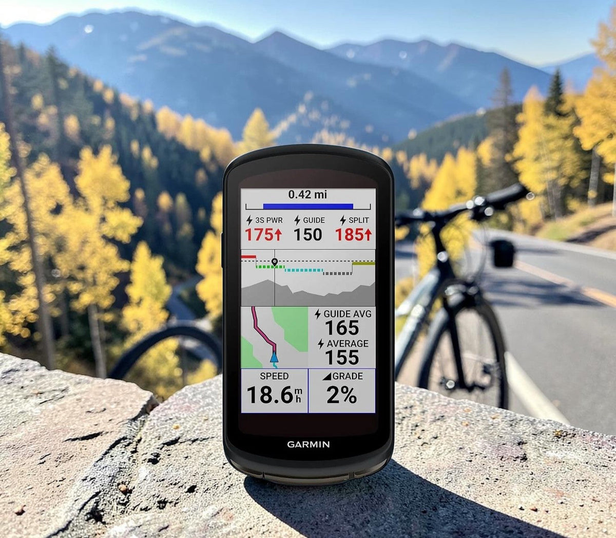 Garmin Edge bike computer on a stone wall above a winding mountain road in autumn.