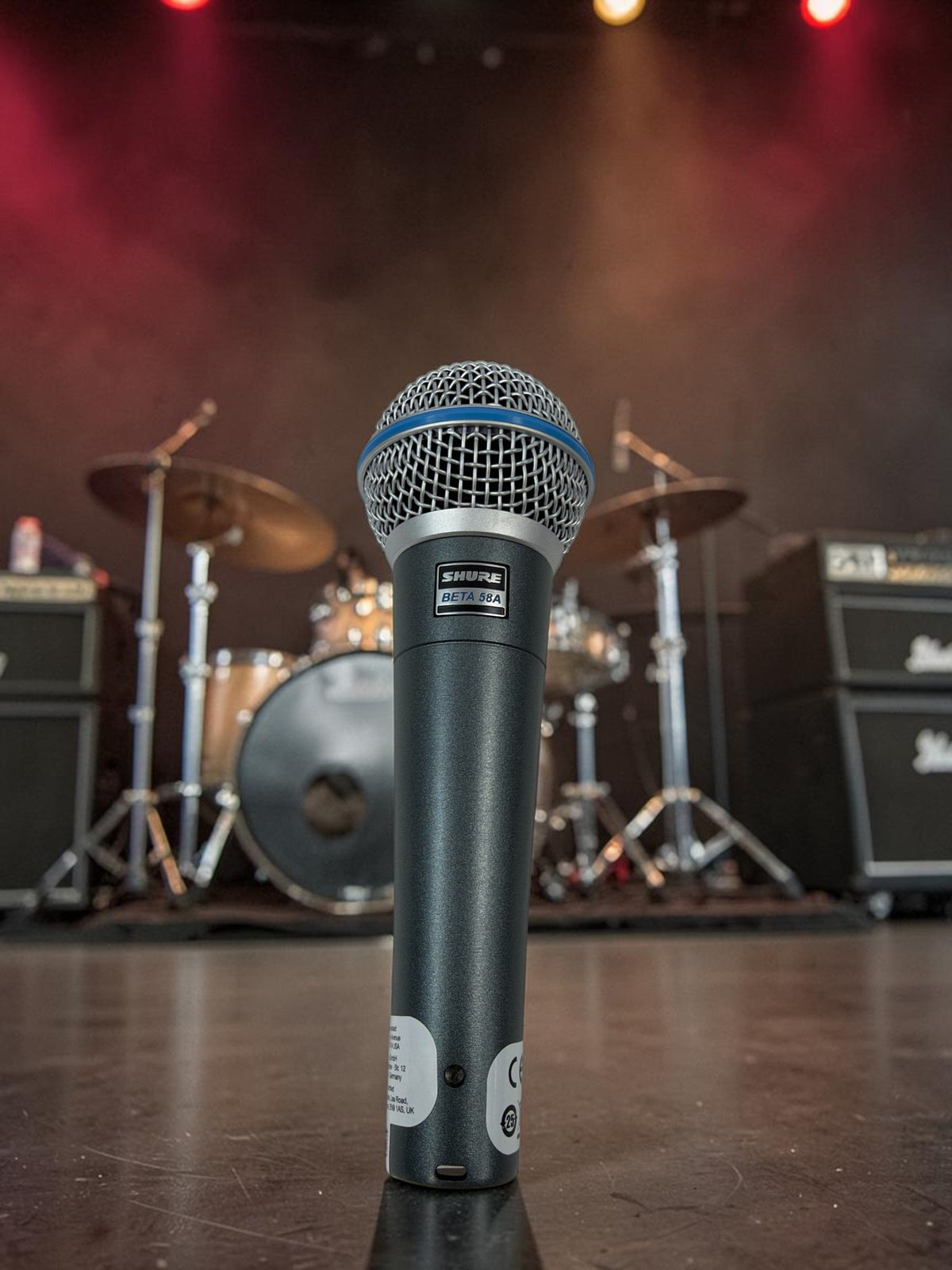 Shure BETA 58A vocal microphone on a rock club stage lit with red and amber stage lights.